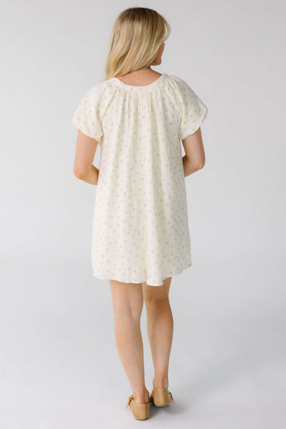 Back view of a woman wearing a cream with blue print  mini dress with short balloon sleeves.