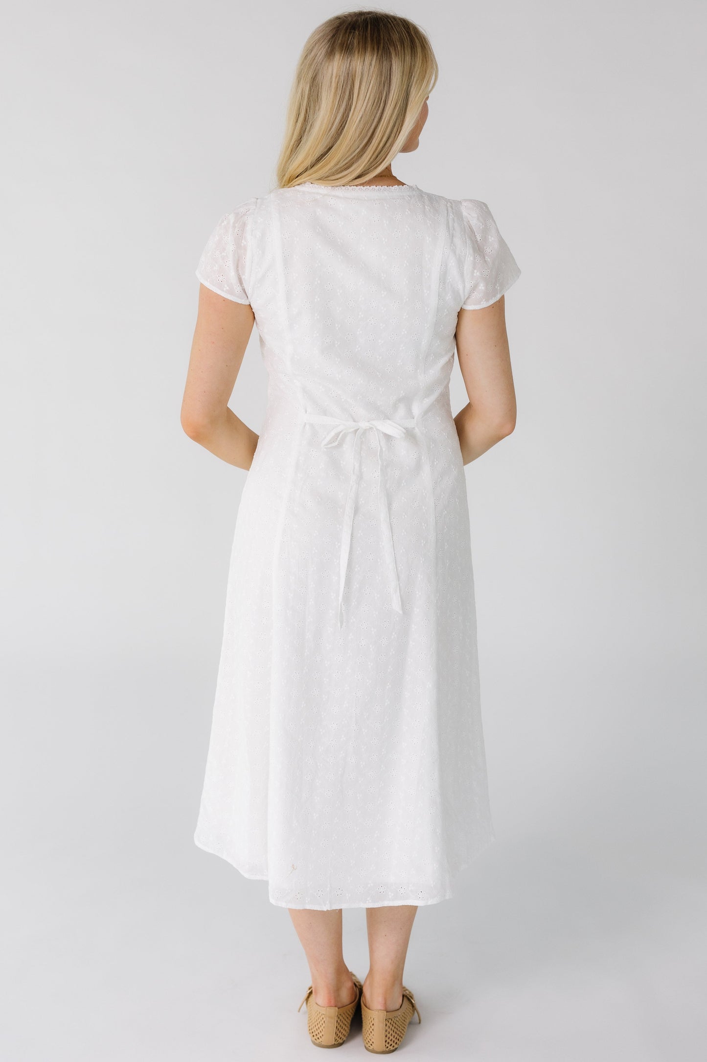 Back view of a woman wearing a white eyelet midi dress with back ties.
