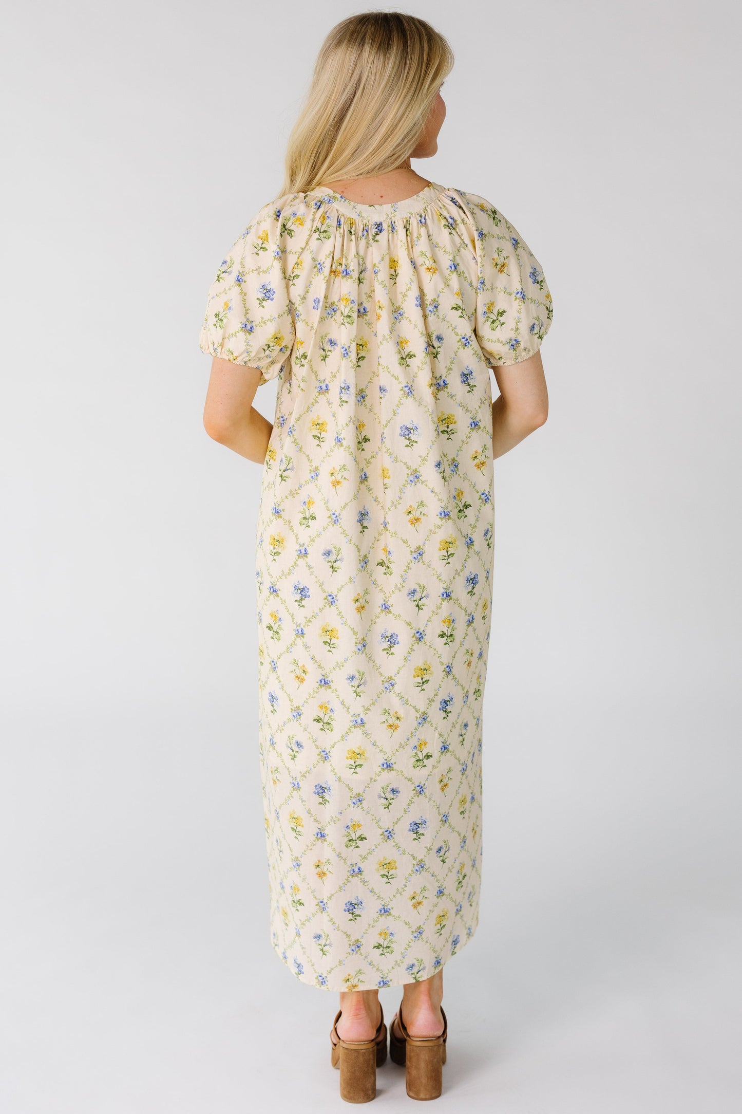 Back view of woman wearing a loose fitting midi dress with a gathered neckline and short balloon sleeves.