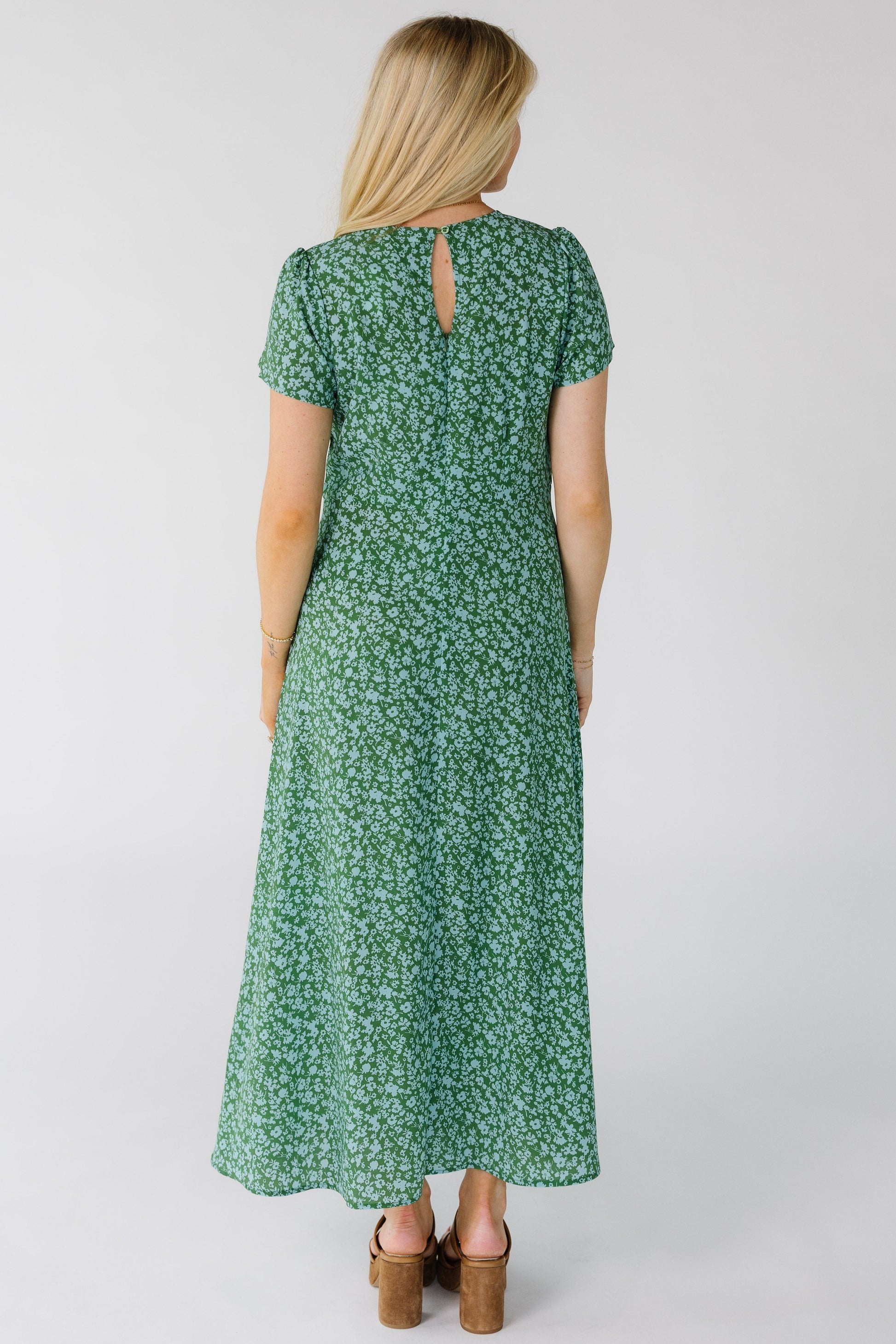 Back view of a woman wearing a green and light blue floral print midi dress with  short sleeves.