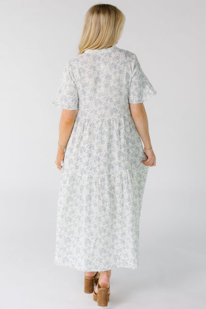 Back view of a woman wearing a white midi dress with blue floral print and short sleeves.