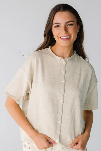 Young woman wearing a modest beige-oatmeal button down cardigan with a rolled neckline, and short sleeves.