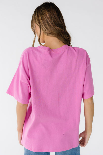 Back view of a woman wearing a short sleeve bright pink tee that is loose fitting.