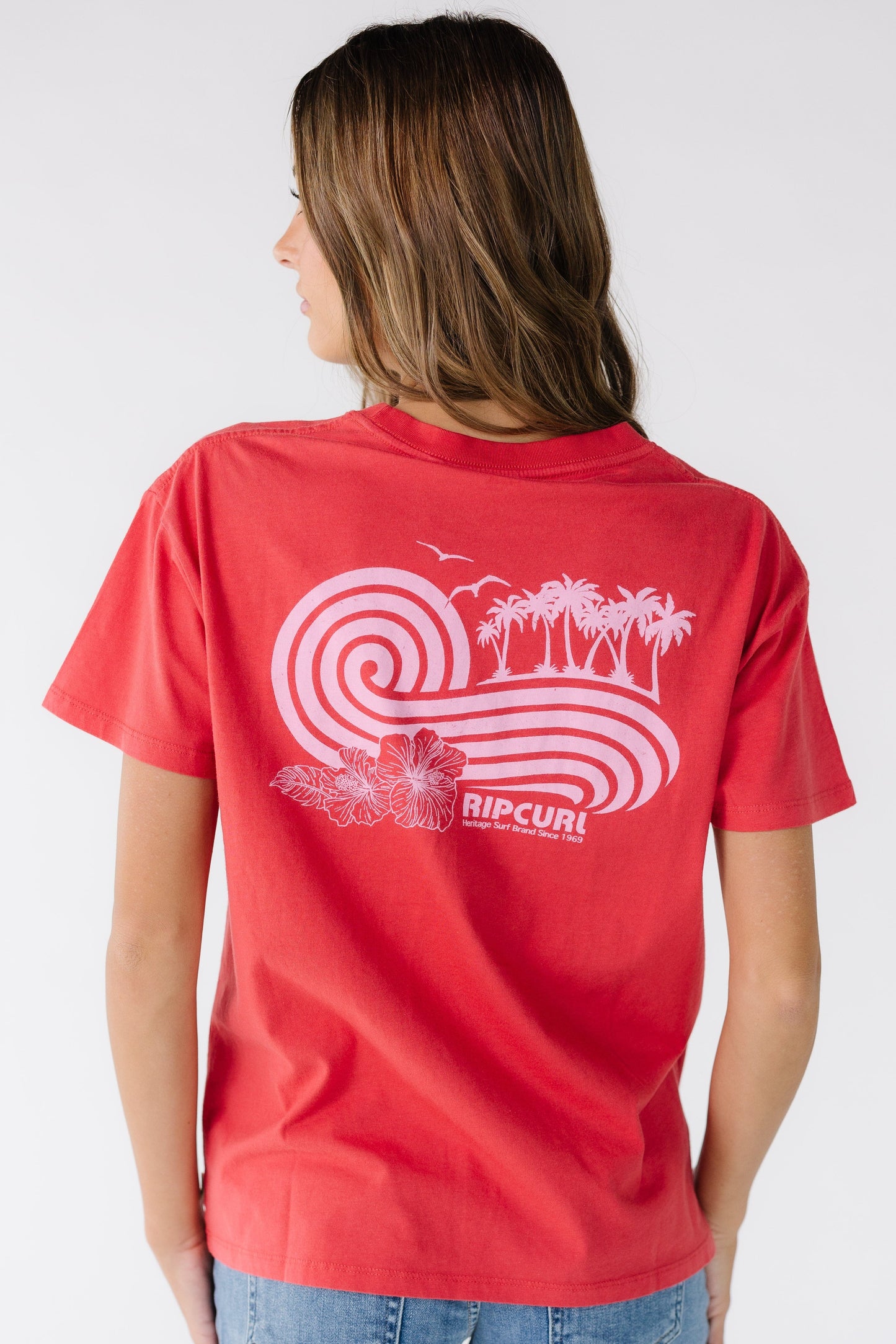 Back view of a young woman wearing a red Rip Curl graphic tee with a large back graphic.