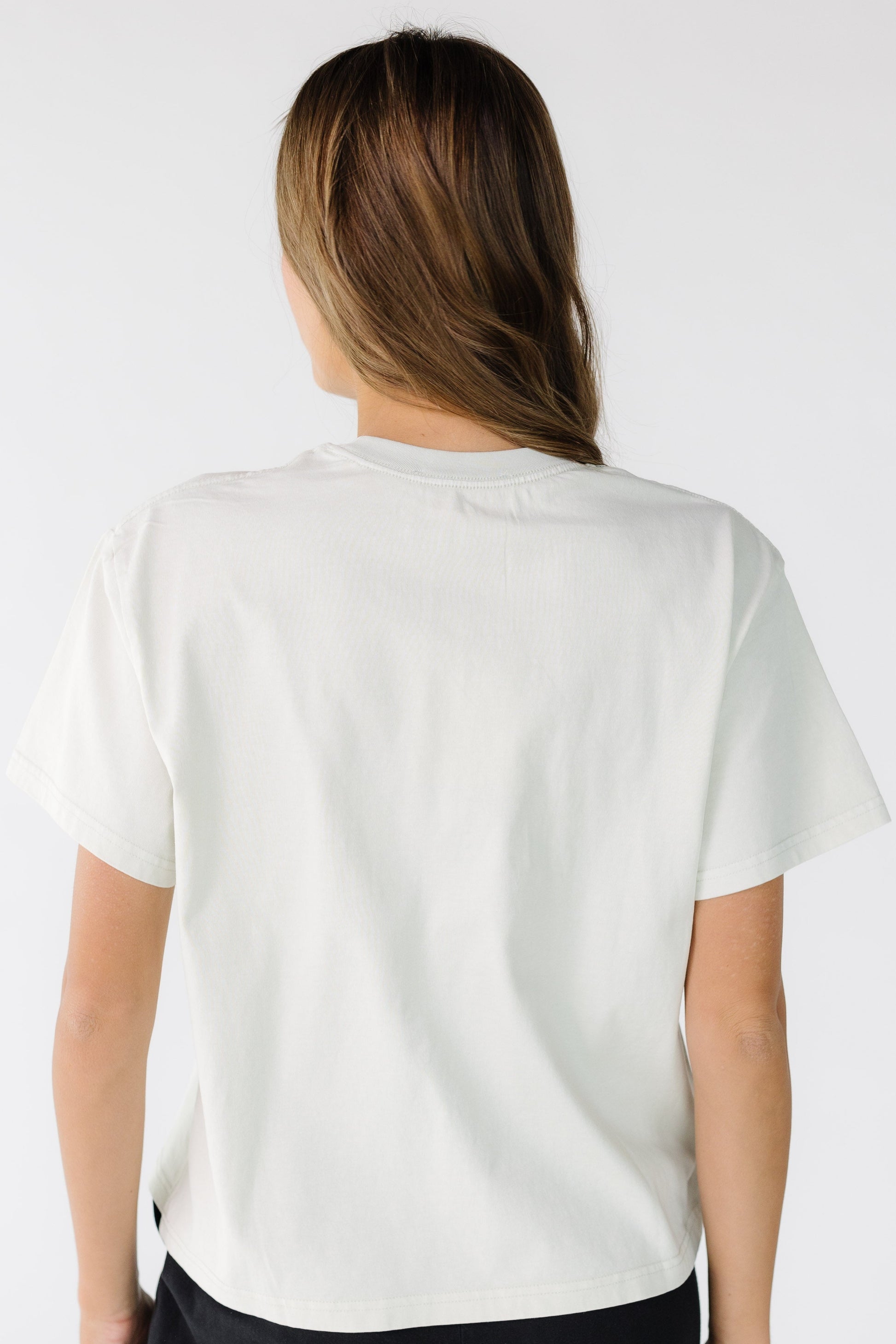 Back view of a young woman wearing an off white tee with short sleeves.