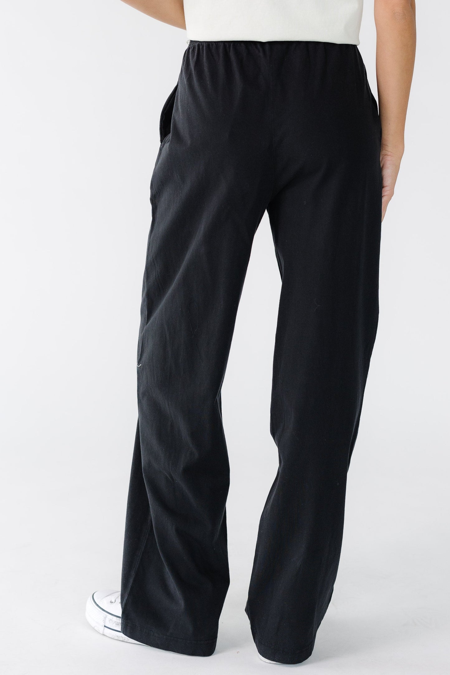 Back view of a women wearing a pair of black wide leg pants with side pockets.