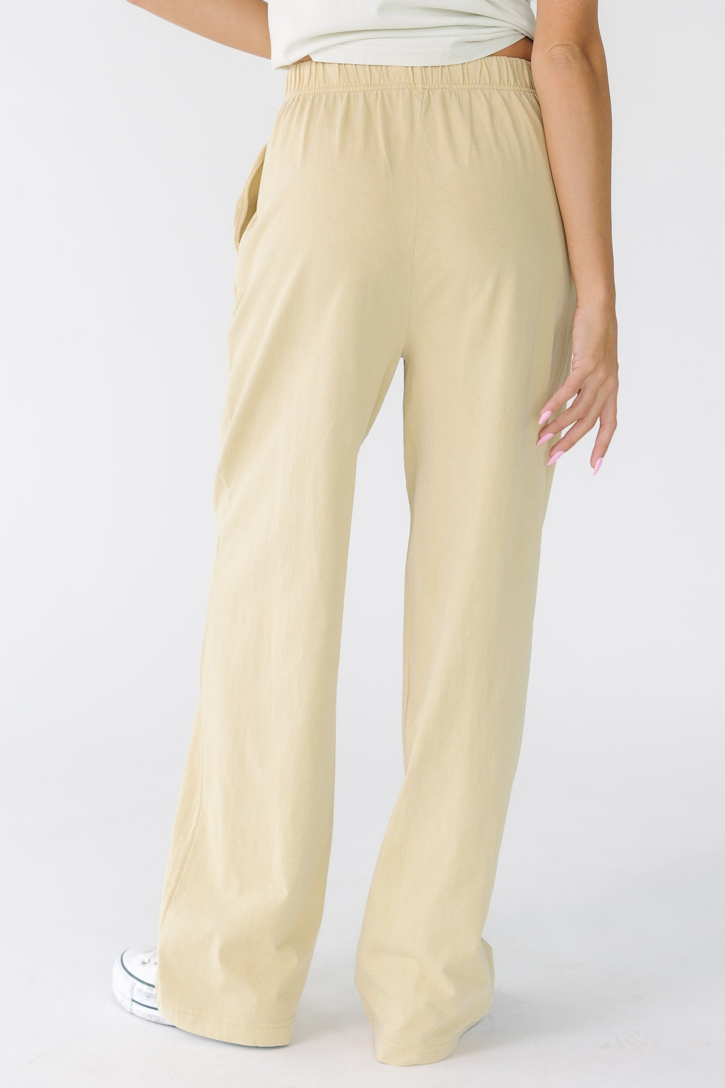 Back view of a woman wearing a pair of beige loose fitting pants with side pockets.
