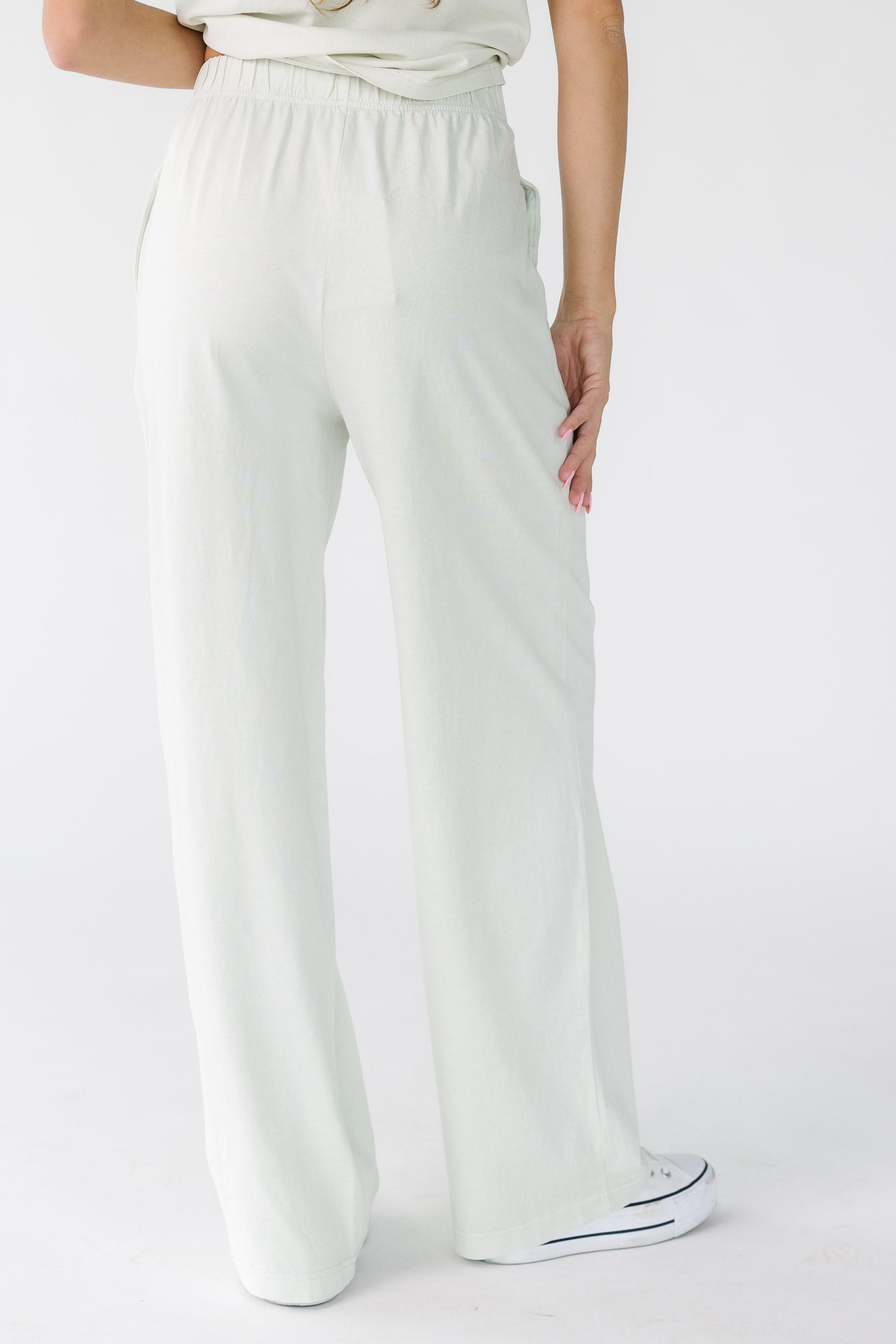 Back view of a woman wearing a pair of loose fitting pants with an elastic waistband and side pockets.