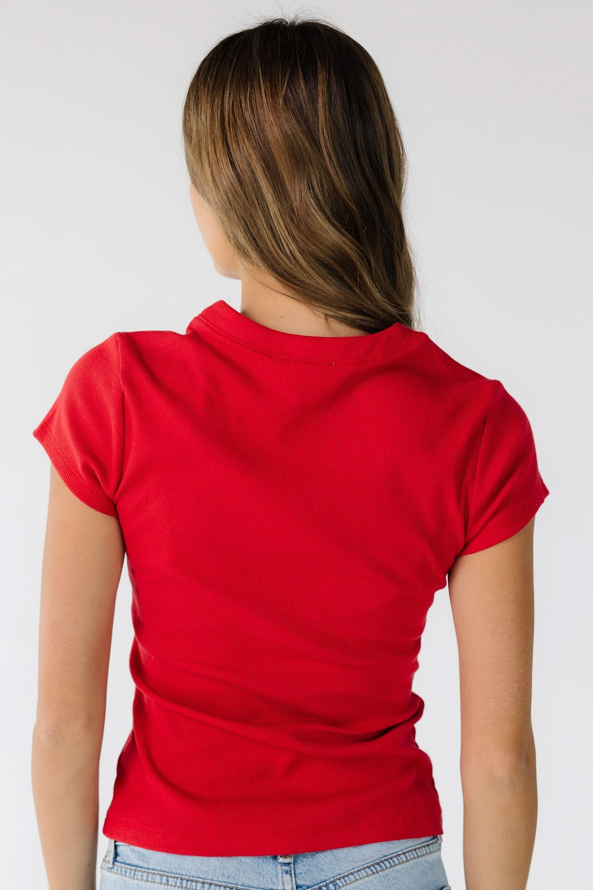 Back view of a woman wearing a red knit top with short sleeves and a round neckline.