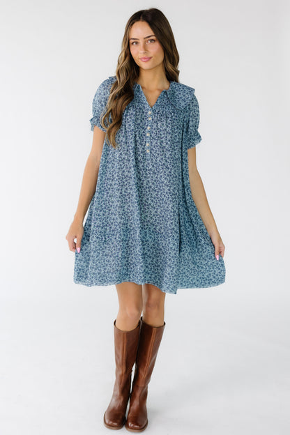 Woman wearing a modest blue floral print dress with a V-neckline, rounded collar and smocked front and back yoke.