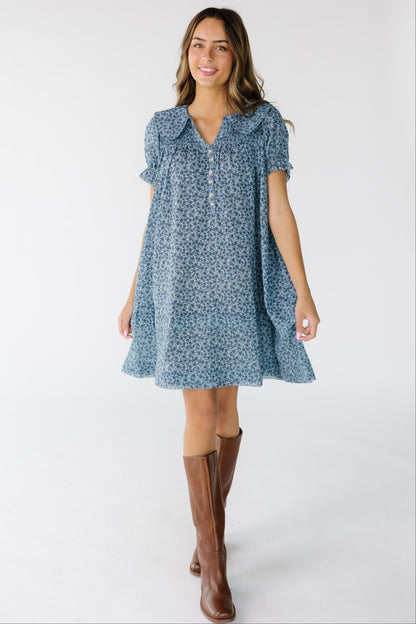 Woman wearing a short blue floral print dress that is loose fitting with a V-neckline.