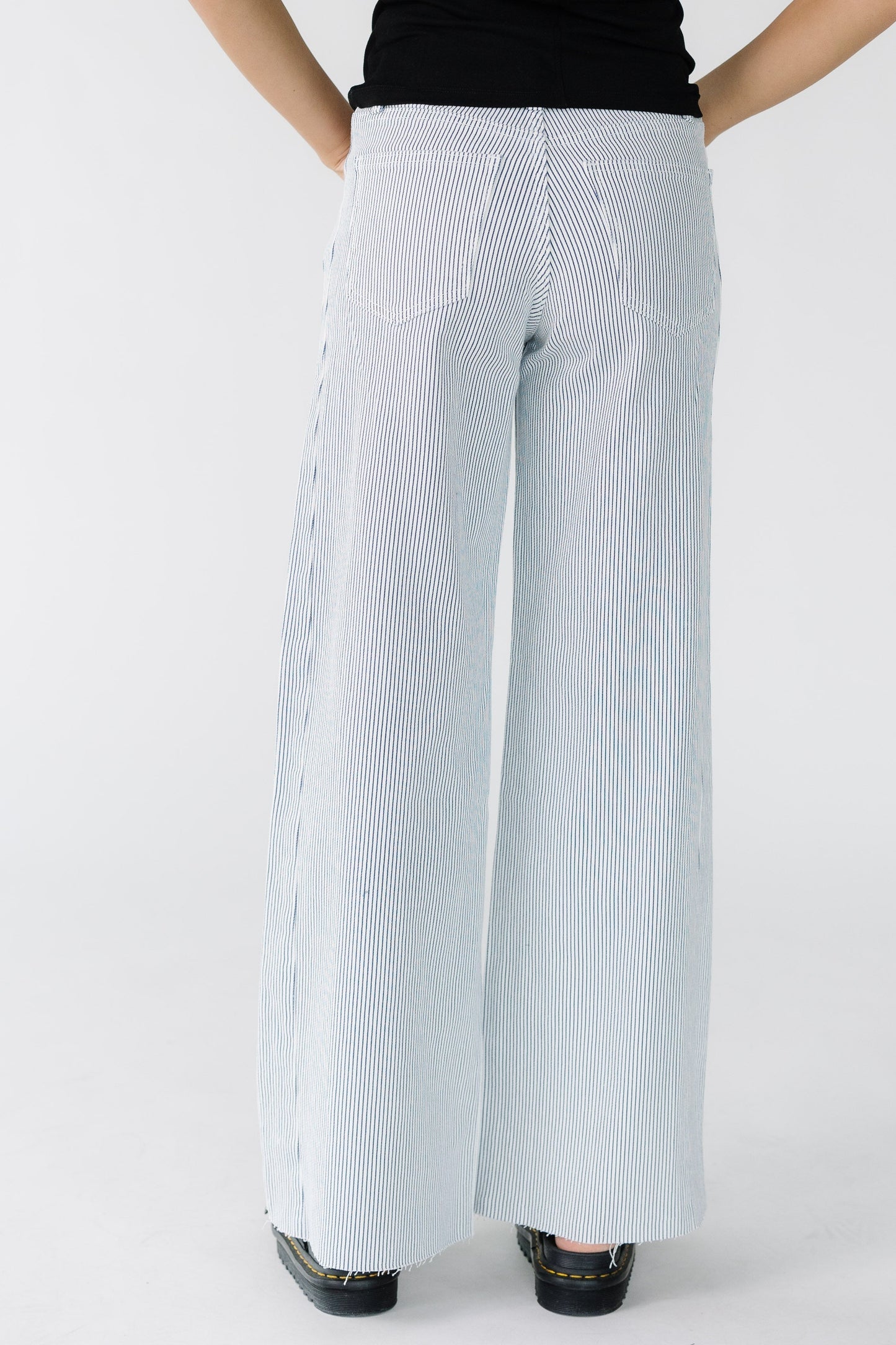 Back view of a woman wearing white wide leg jeans with thin navy stripes.