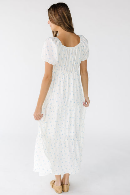 Back view of a woman wearing a white and blue floral print midi-maxi dress with short sleeves.