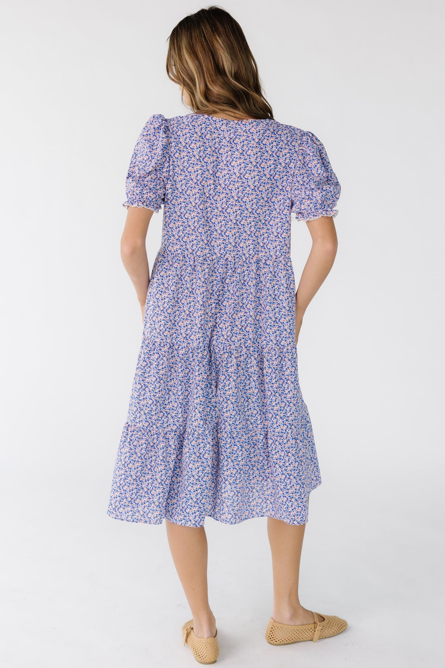 Back view of a woman wearing a loose fitting purple floral dress that is below knee length.