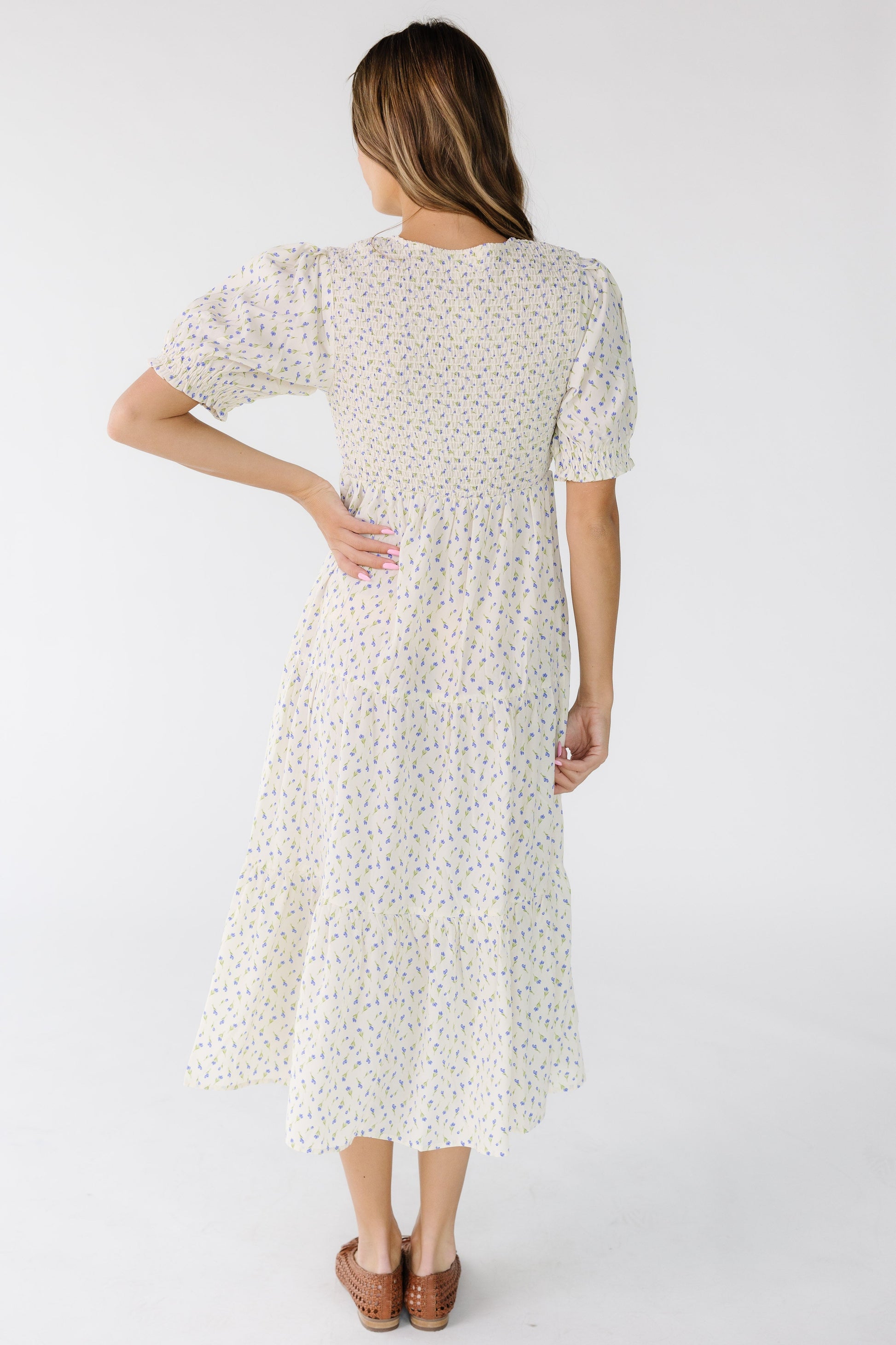 Back view of a woman wearing an ivory floral print midi dress with a smocked back bodice and short sleeves.