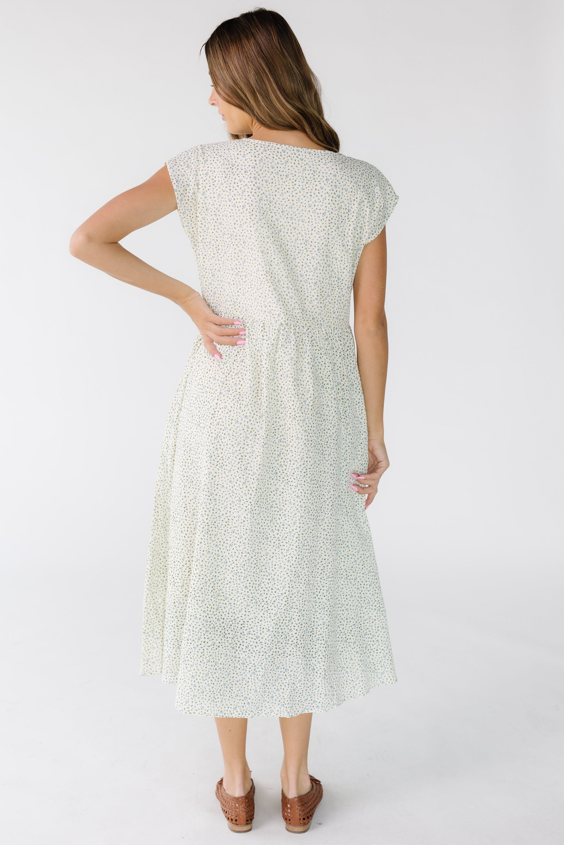 Back view of a woman wearing a white floral print midi dress with short sleeves and a gathered skirt.