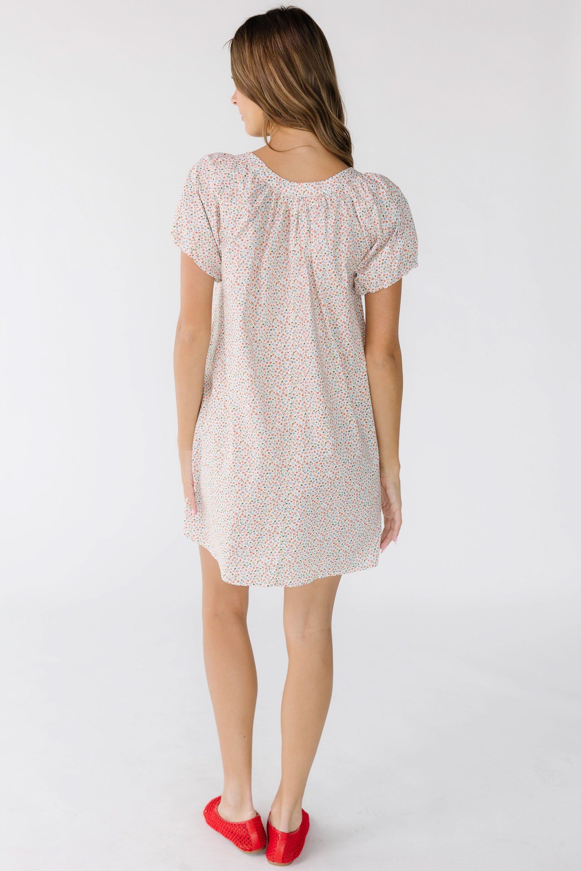 Back view of a woman wearing a white floral, short dress with puff sleeves.