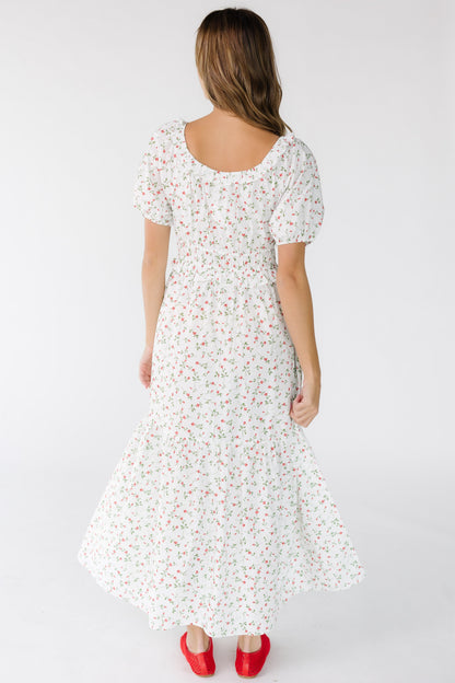 Back view of a young woman wearing an ivory and red floral print dress with a full skirt and short sleeves.