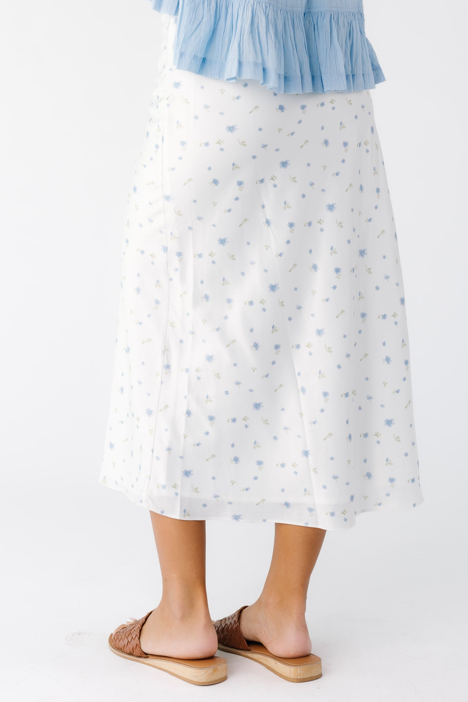Back view of a woman wearing an off white A-line midi skirt with a blue scattered floral print.