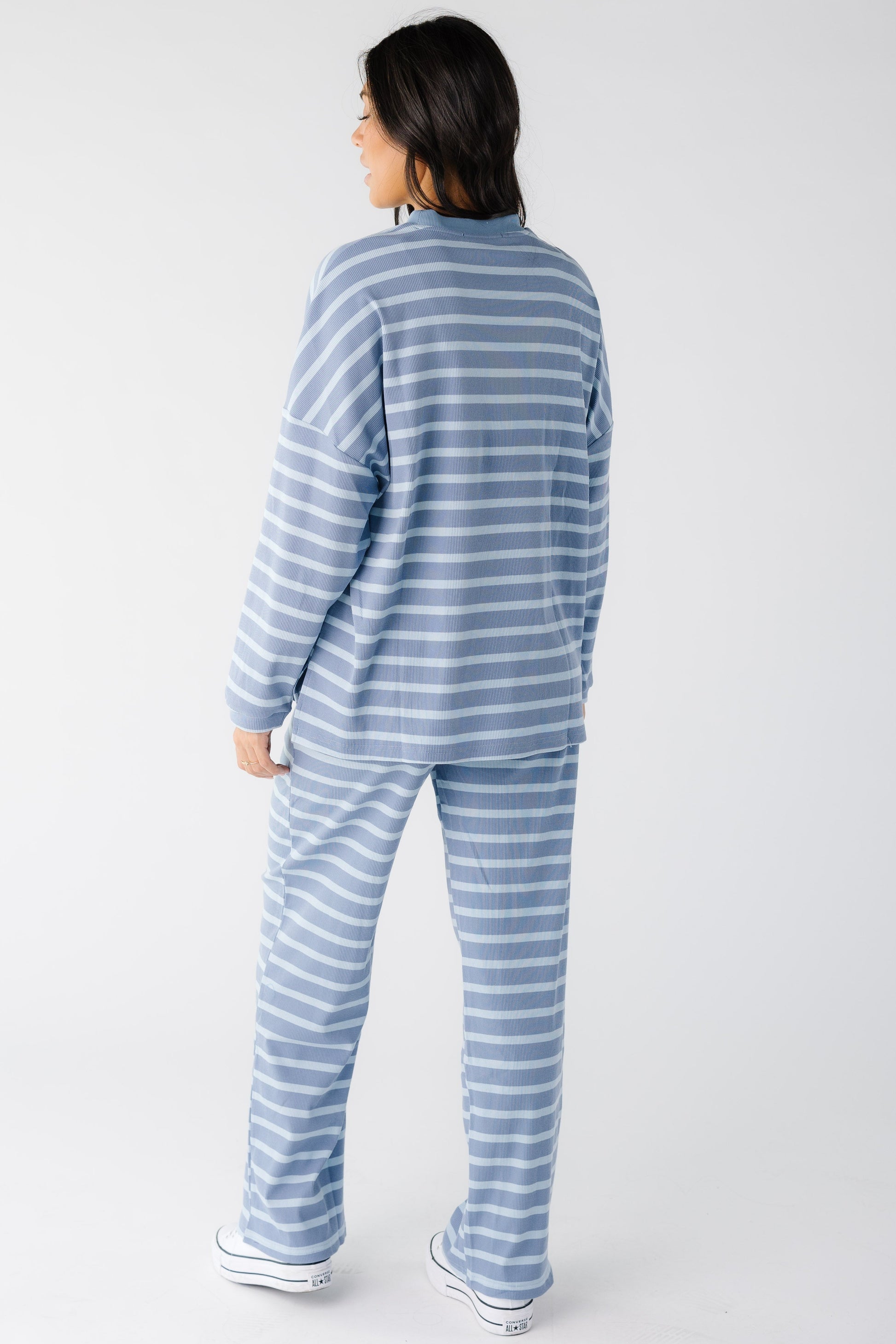 Back view of a young woman wearing a light blue cotton ribbed lounge set with long sleeves and long wide cut leg.