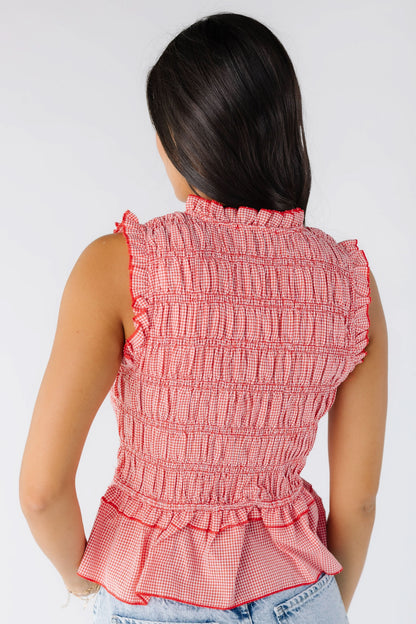 Back view of a young woman wearing a red and white small gingham smocked top that is sleeveless with a bottom ruffle peplum.