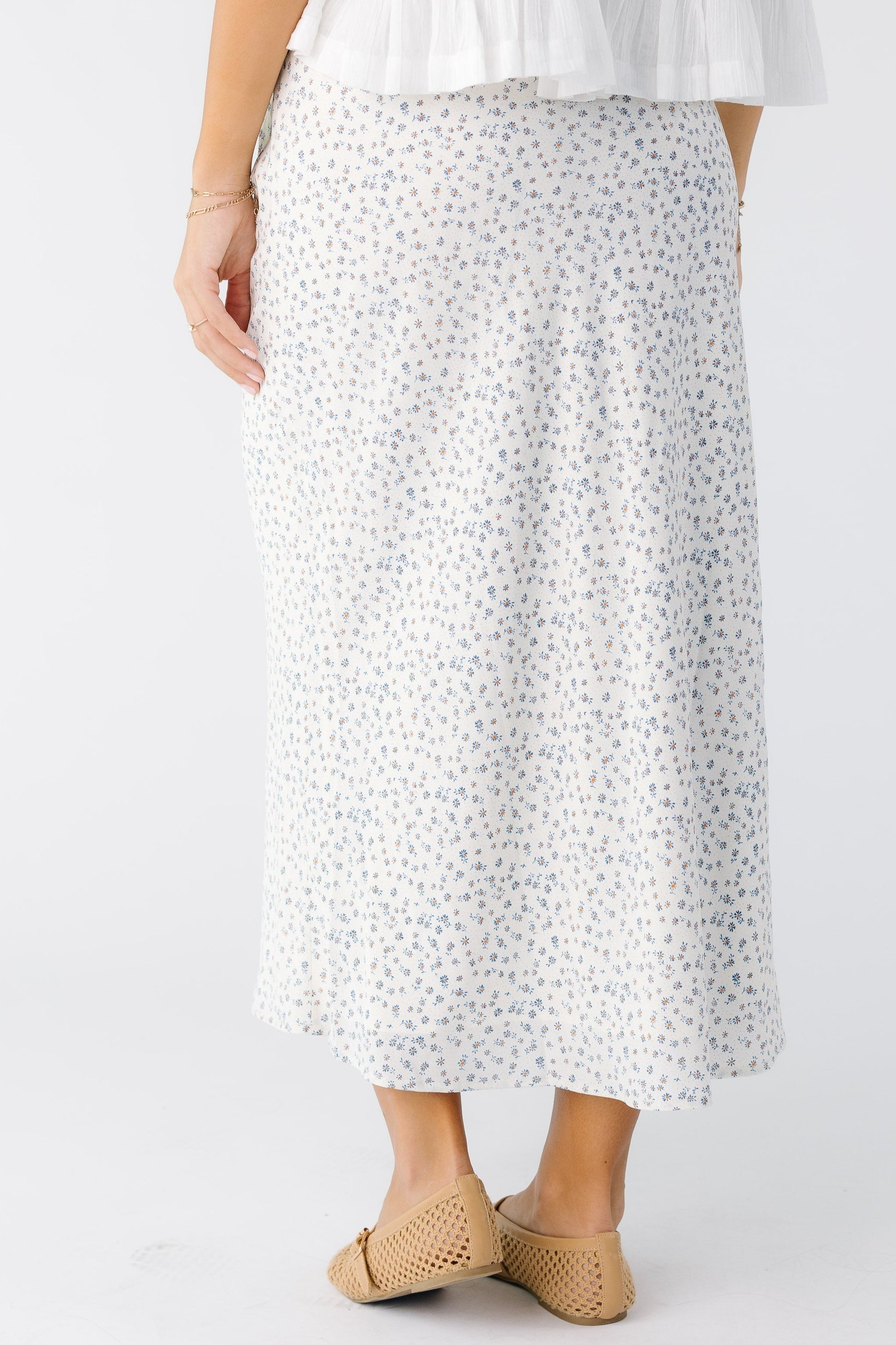 Back view of a young woman wearing a white with dainty blue floral printA-line skirt.