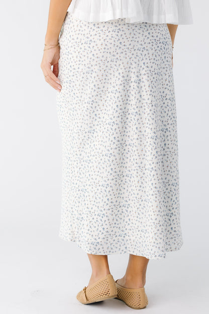 Back view of a young woman wearing a white with dainty blue floral printA-line skirt.