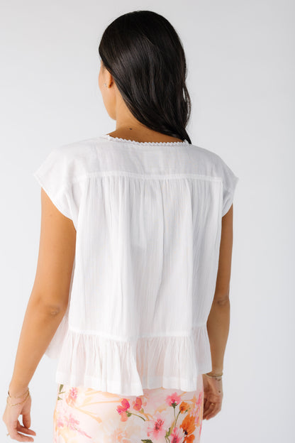 Back view of a young woman wearing a white short sleeve, loose fitting blouse with a bottom ruffle.