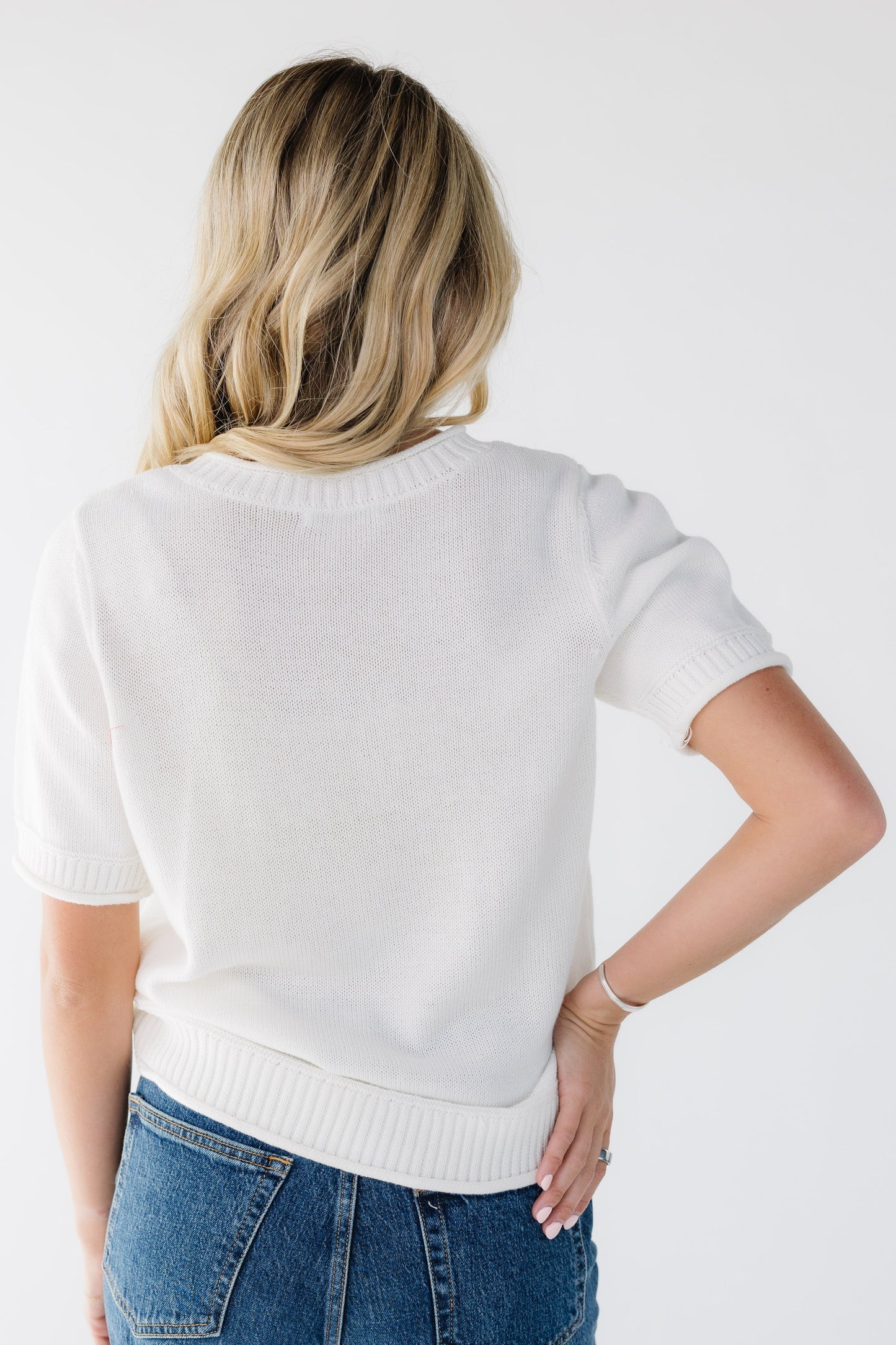 Back view of a young woman wearing an off white sweater with short sleeves.