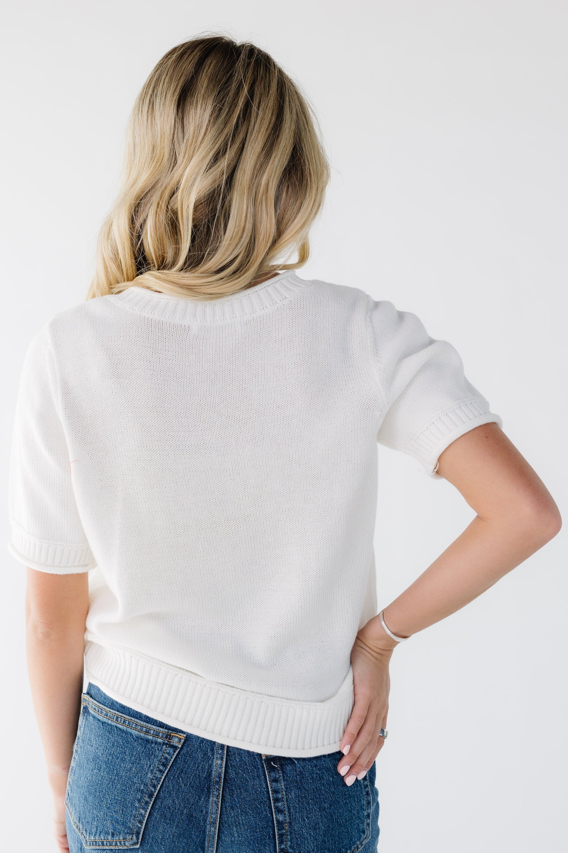 Back view of a young woman wearing an off white sweater with short sleeves.