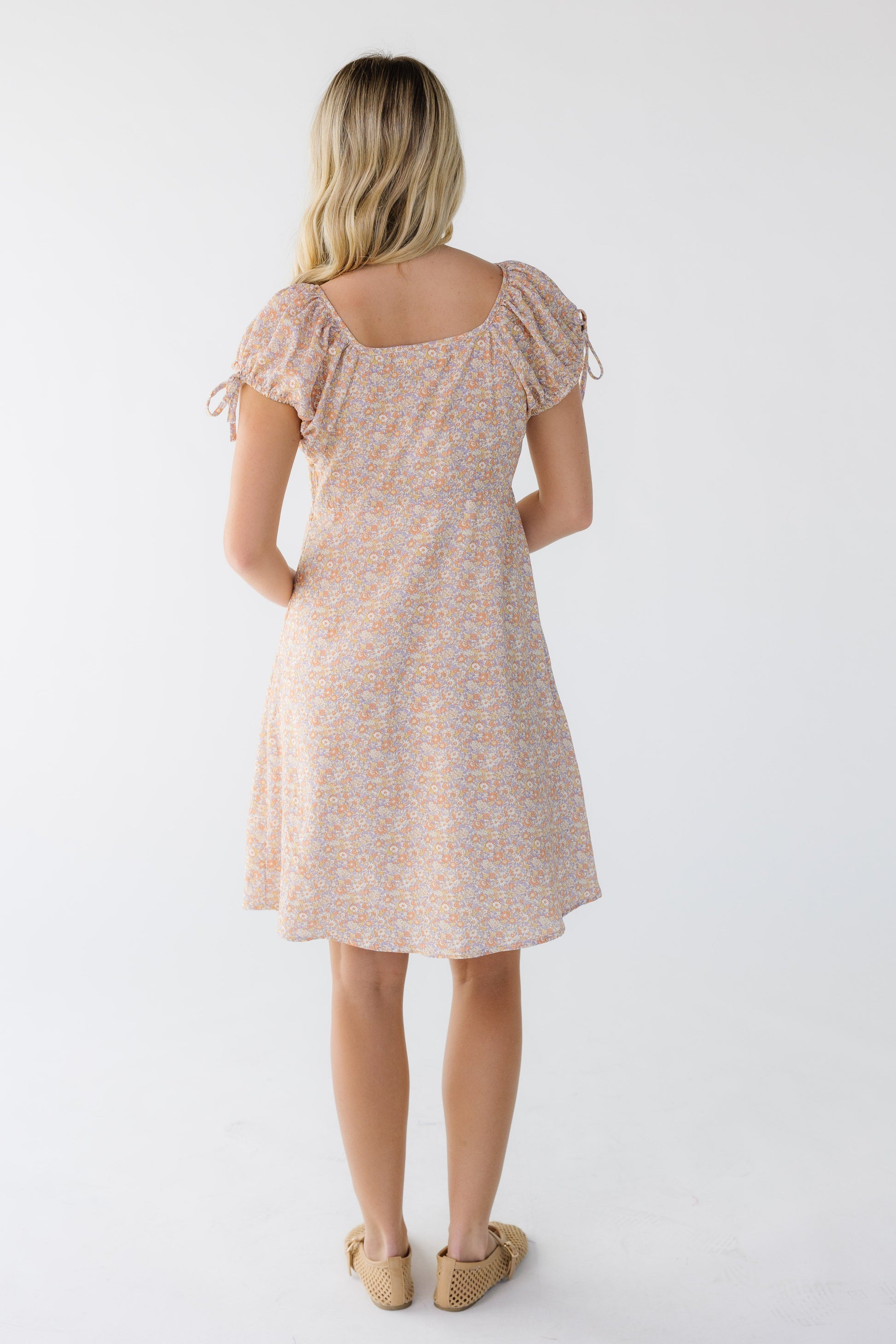 Back view of a woman wearing a pink multi color knee length dress with short puff sleeves.