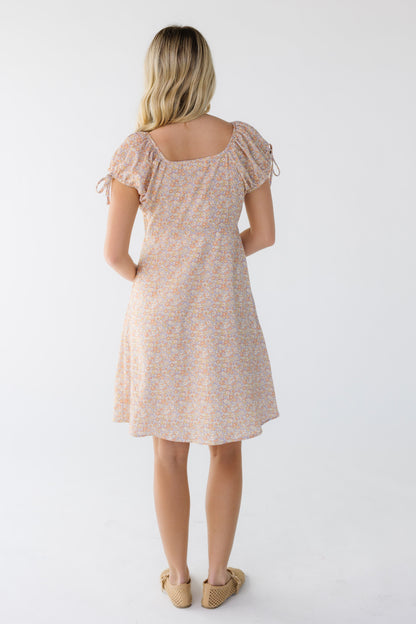 Back view of a woman wearing a pink multi color knee length dress with short puff sleeves.