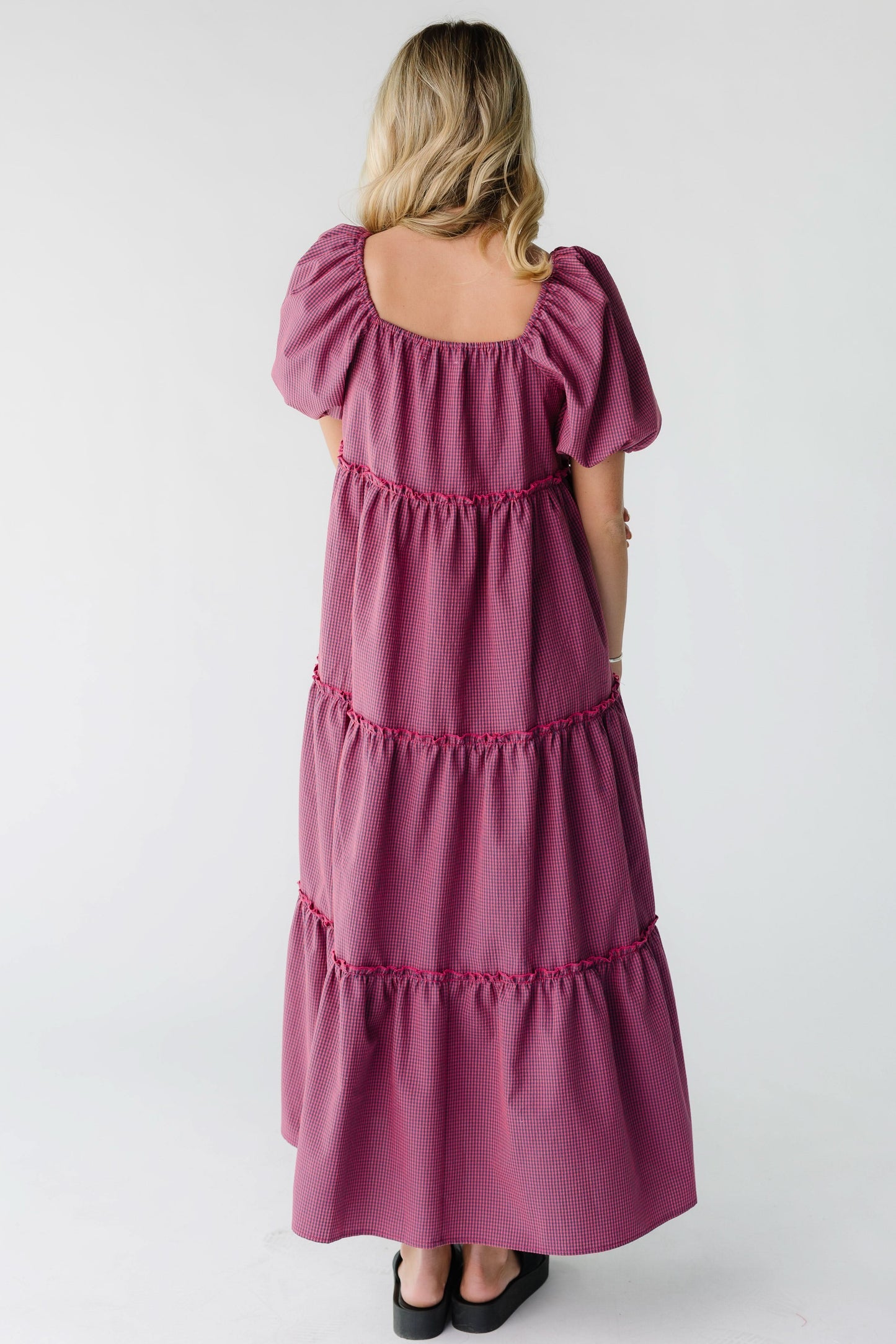 Back view of a woman wearing a loose fitting midi-maxi tiered dress with balloon sleeves and a square neckline.