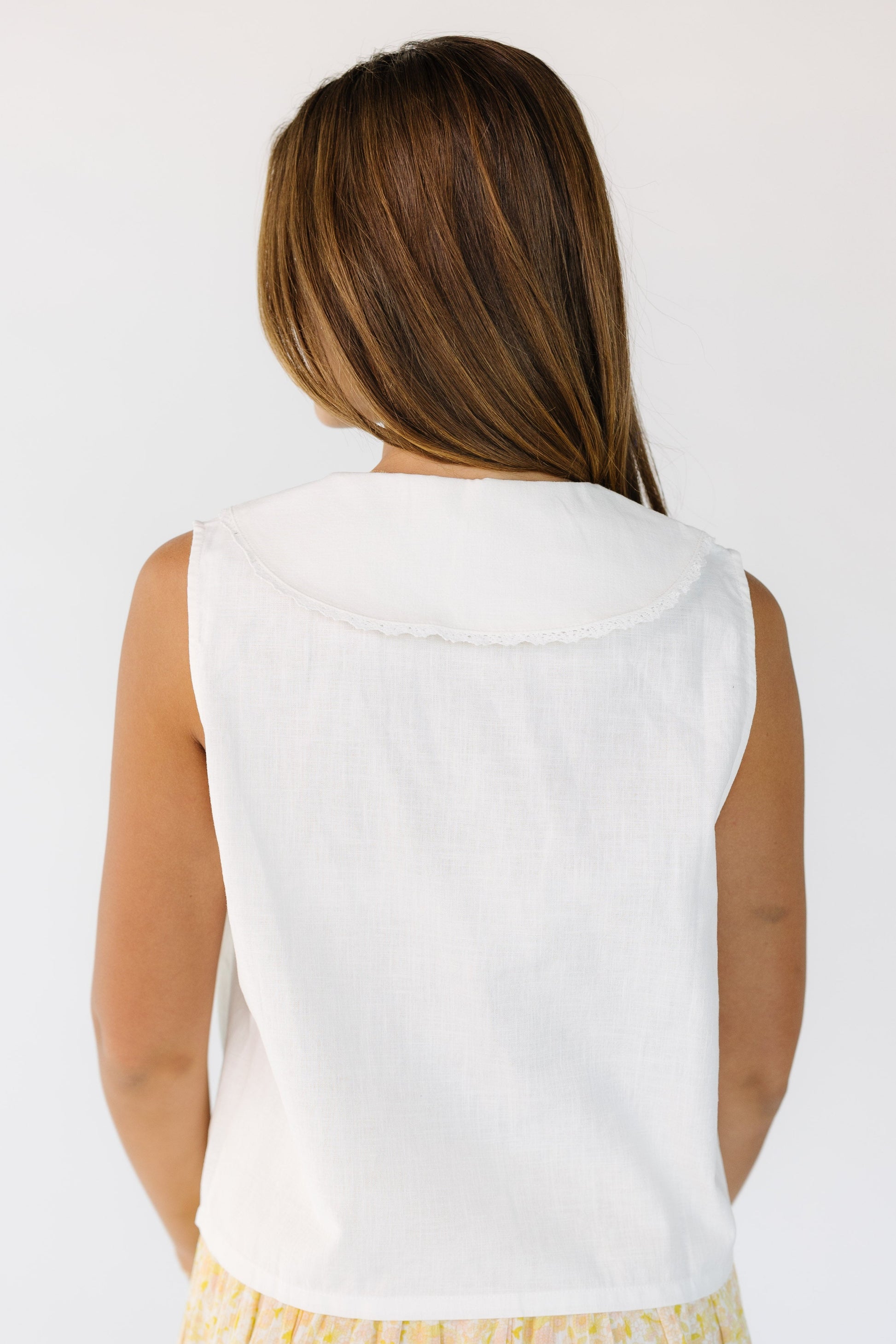 Back view of a woman wearing a white sleeveless top with a lace edge shawl collar.