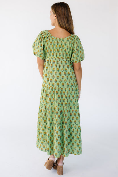 Back view of a woman wearing a green midi dress with short full sleeves and a back slight scoop neckline.