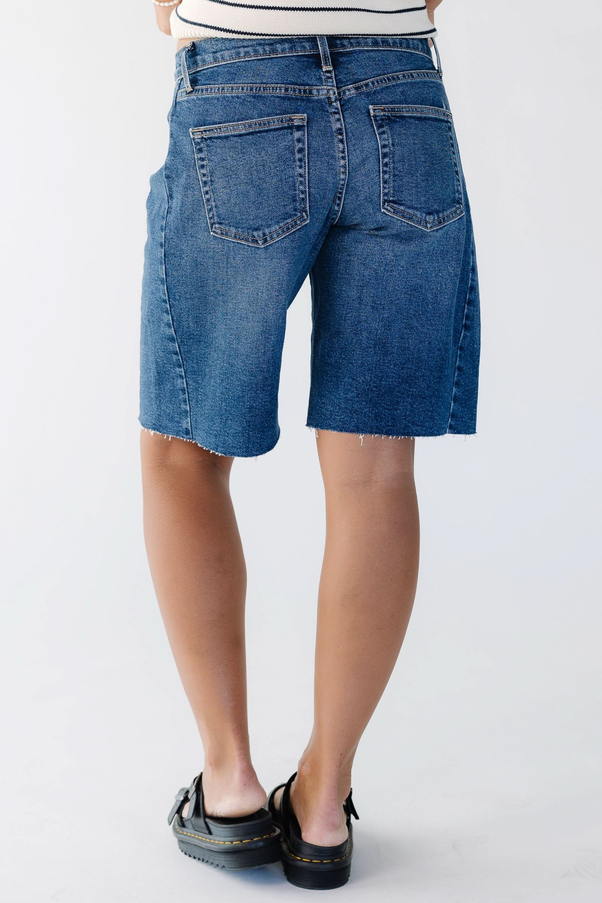 Back view of a woman wearing a pair of dark denim shorts with scissor cut hems.