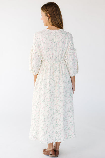 Back view of a woman wearing a cream and pink floral midi dress with half length sleeves.