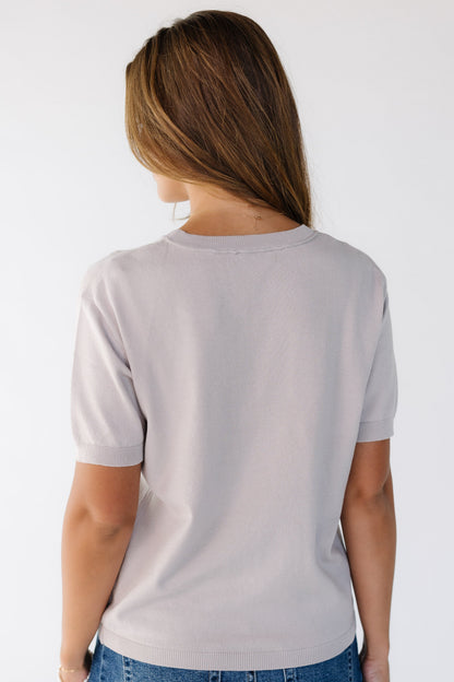 Back view of a young woman wearing a soft lightweight sweater with short sleeves with a crew neckline.
