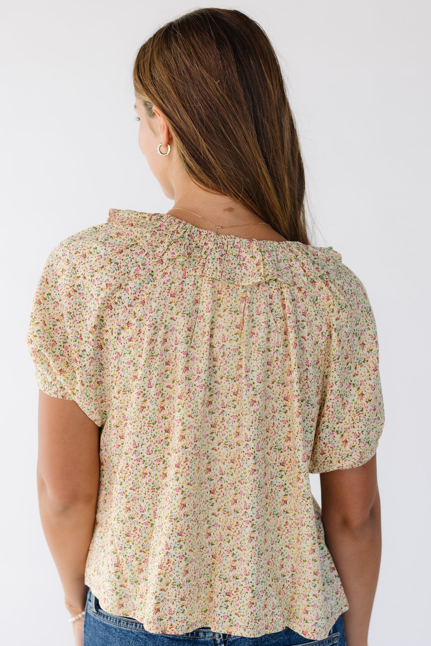 Back view of a woman wearing a yellow print top with short puff sleeves and a ruffled neckline.