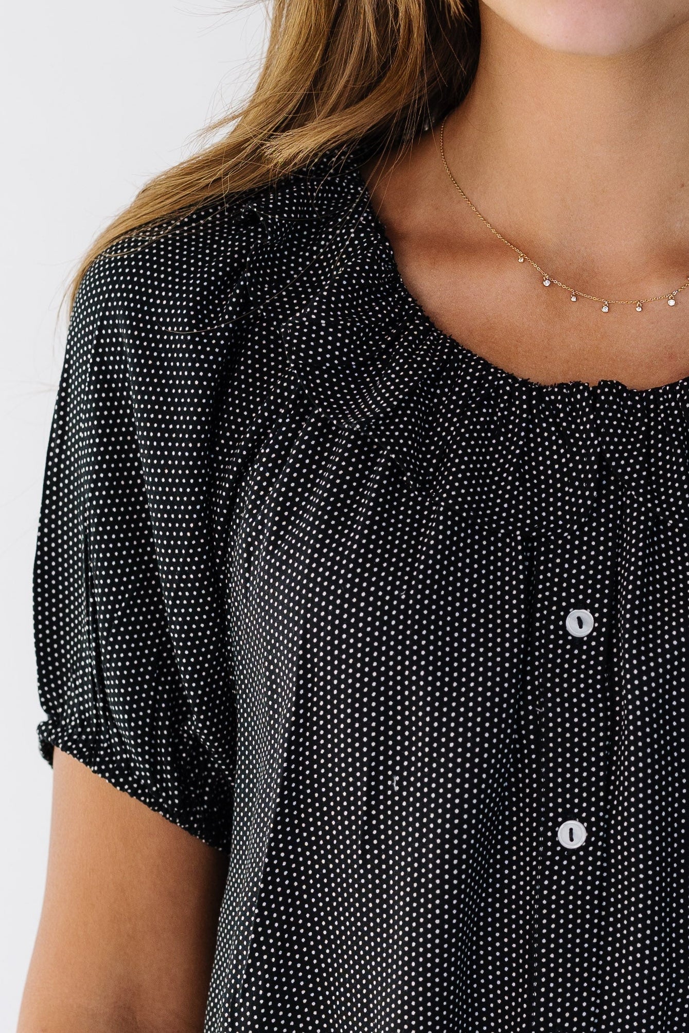 Close view of a woman wearing a black & white polka dot top with a ruffle collar and puff sleeves.