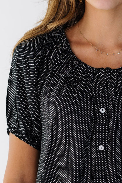 Close view of a woman wearing a black & white polka dot top with a ruffle collar and puff sleeves.