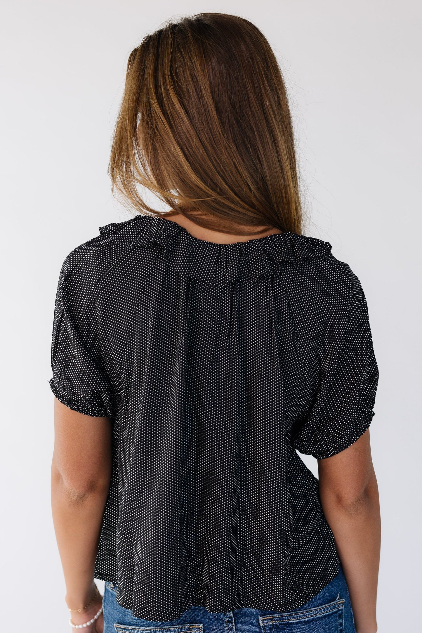 Back view of a young woman wearing a black with white polka dots and short puff sleeves.