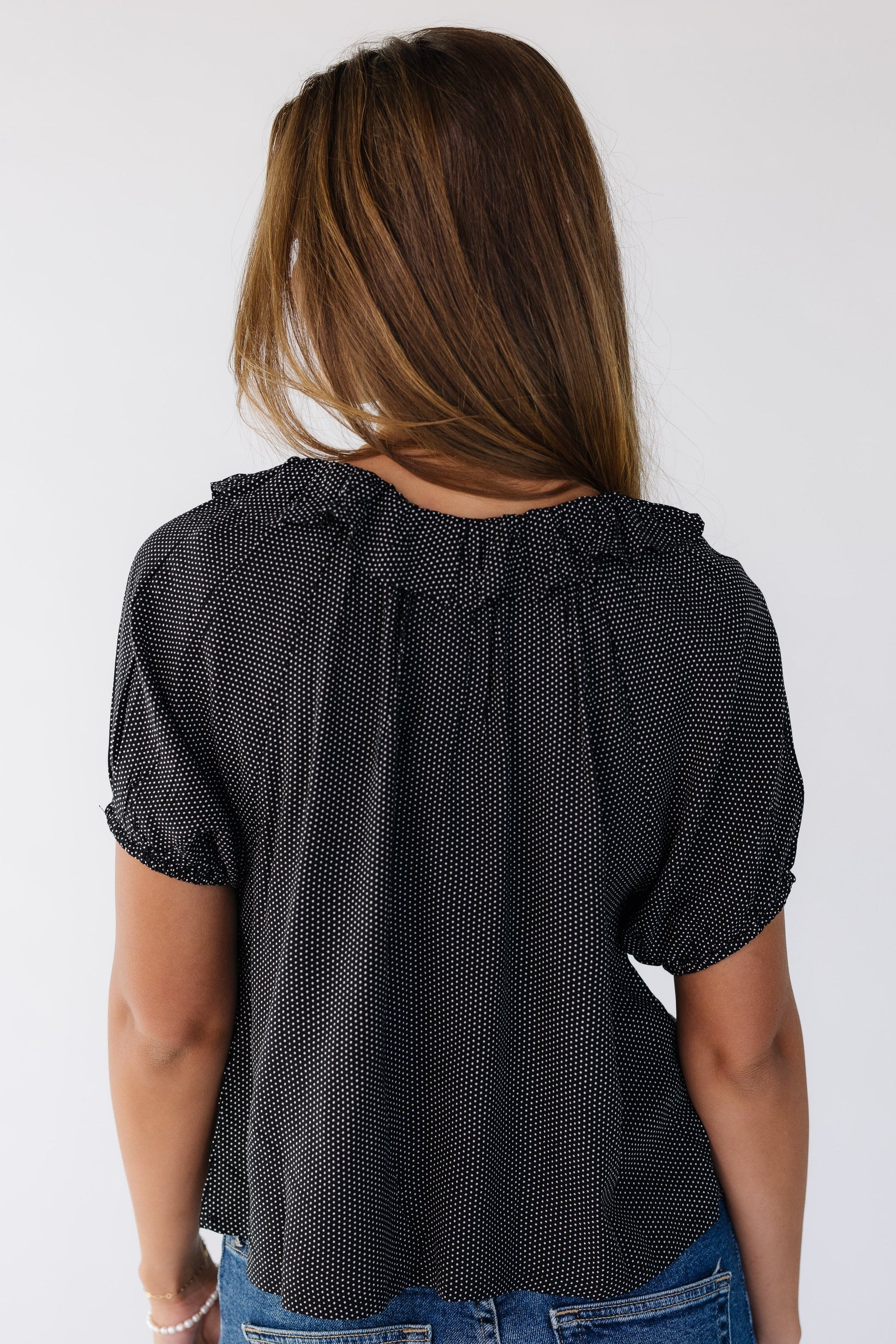 Back view of a young woman wearing a black with white polka dots and short puff sleeves.