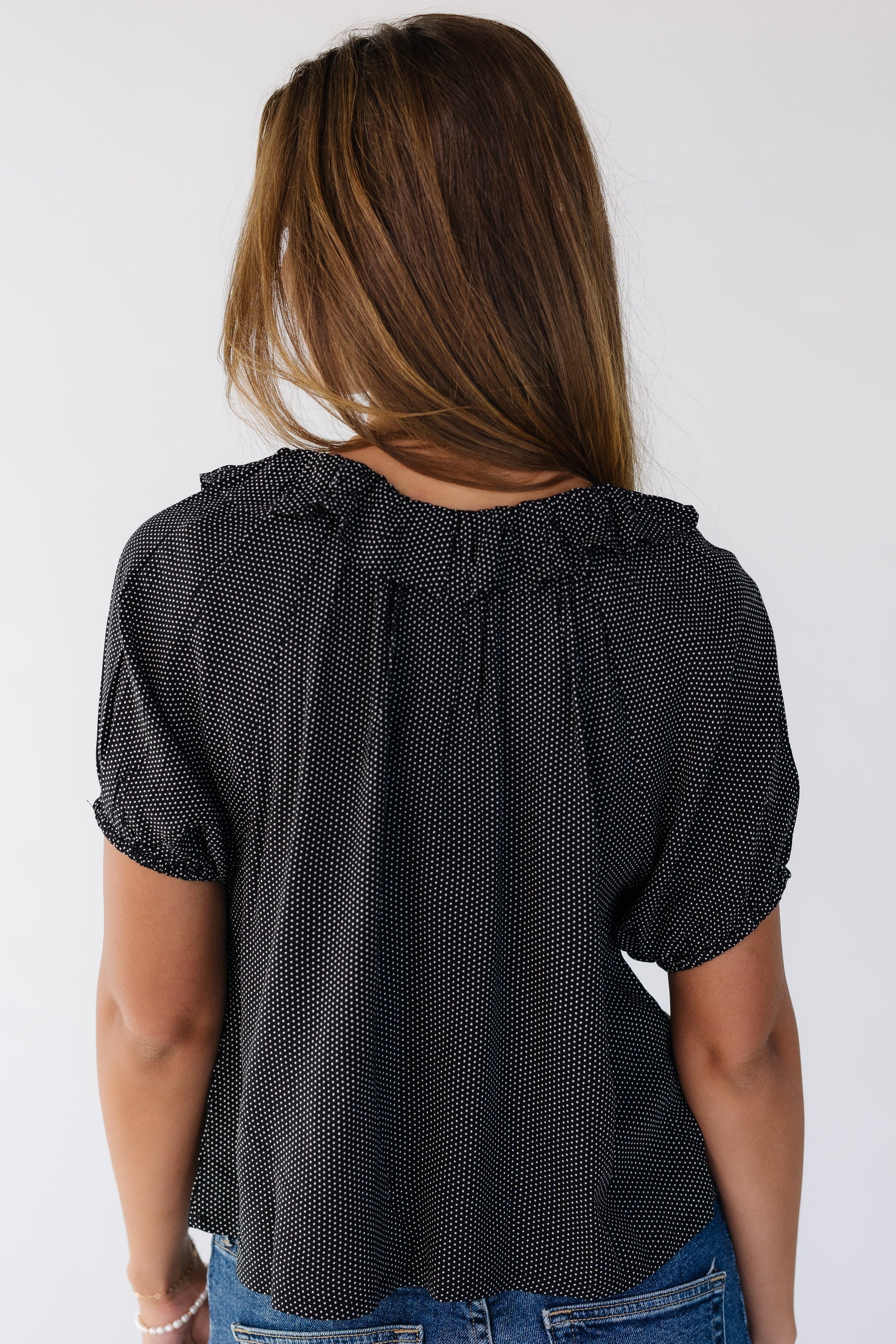 Back view of a woman wearing a loose fitting black polka dot top with short puff sleeves.