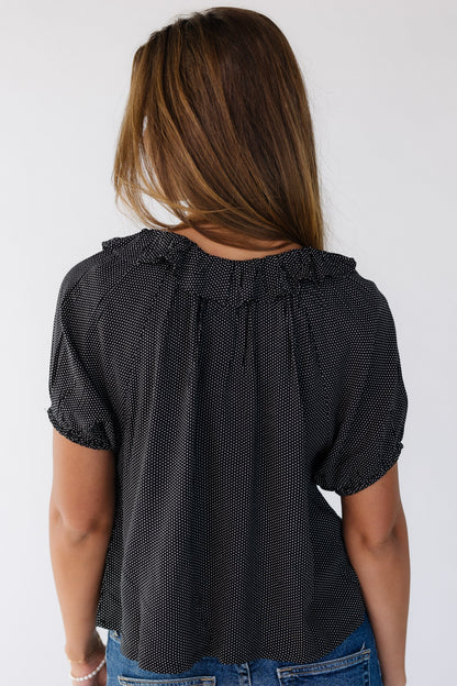 Back view of a woman wearing a loose fitting black polka dot top with short puff sleeves.