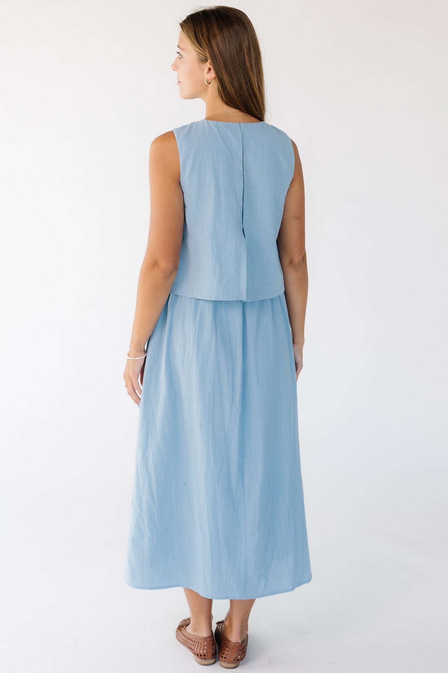 Back view of a woman wearing a sleeveless light fitting 1 piece dress that looks like 2 pieces.