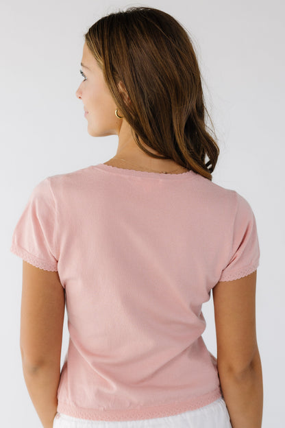 Back view of a woman wearing a pink knit top with scallop hems and short sleeves.