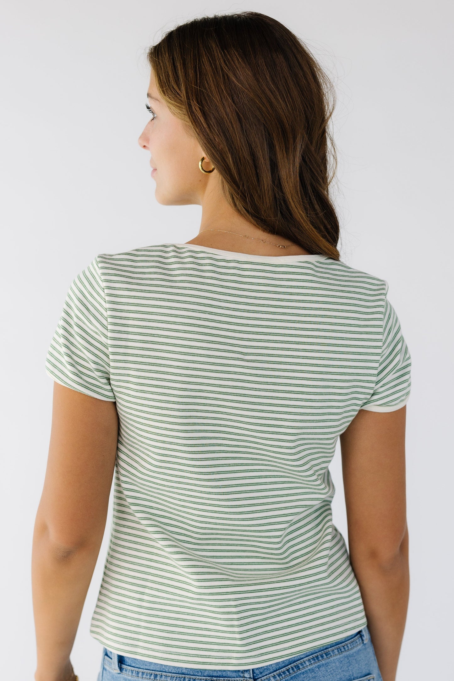 Back view of a woman wearing an ivory and green double stripe closer fitting knit top with short sleeves.