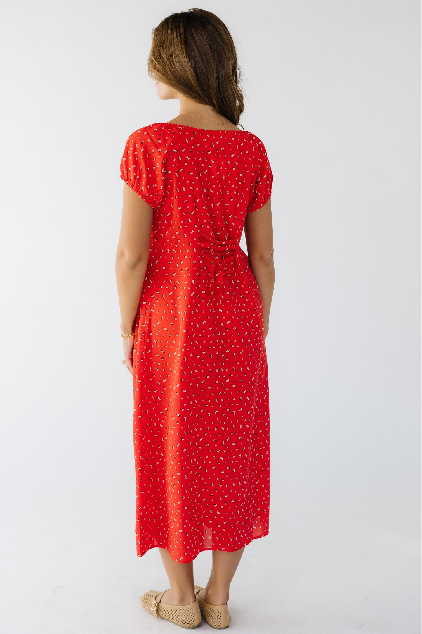 Back view of a woman wearing a loose fitting red midi dress with short puff sleeves and lacing details at the center back to adjust fit.