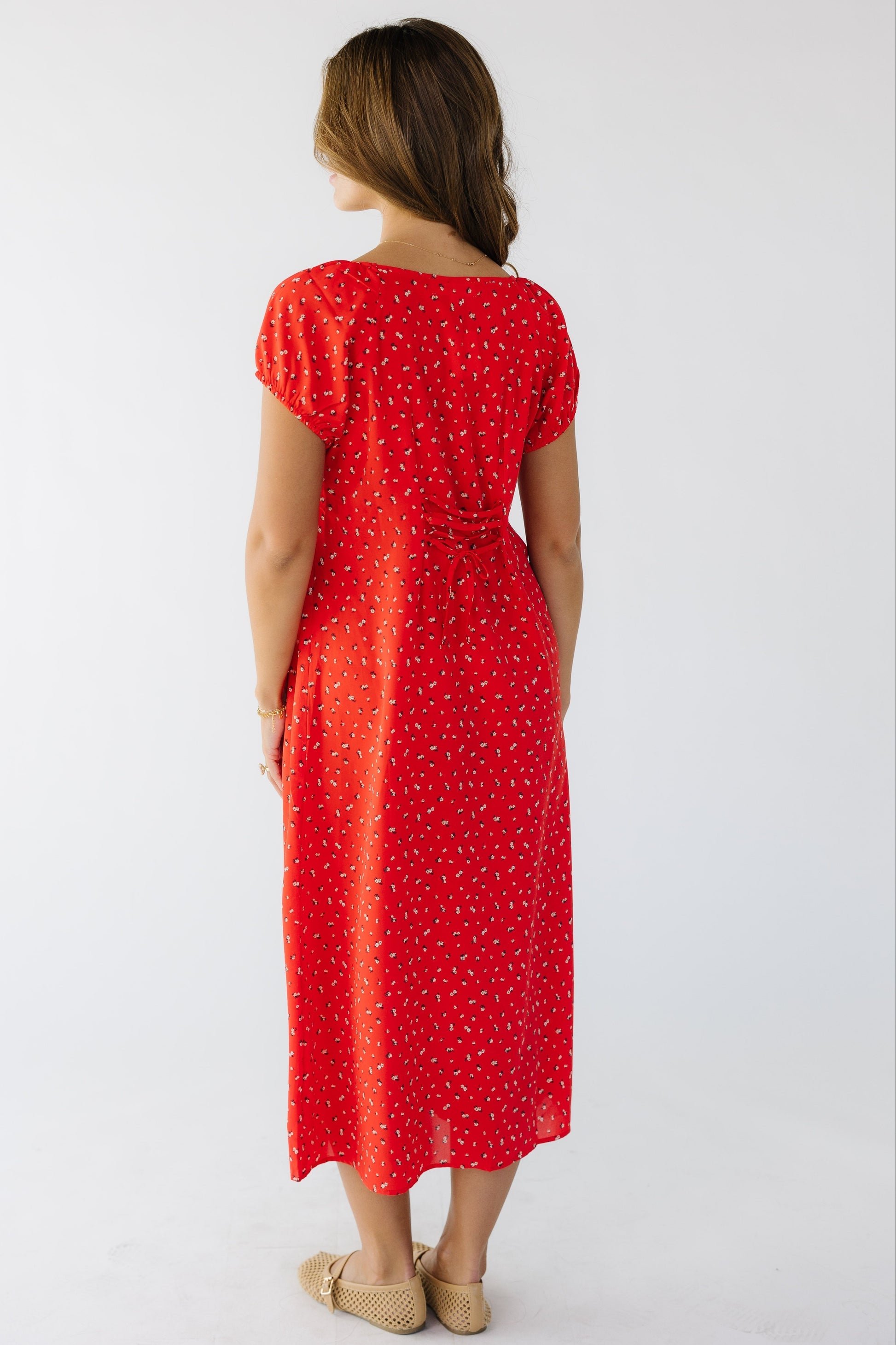 Back view of a woman wearing a loose fitting red midi dress with short puff sleeves and lacing details at the center back to adjust fit.